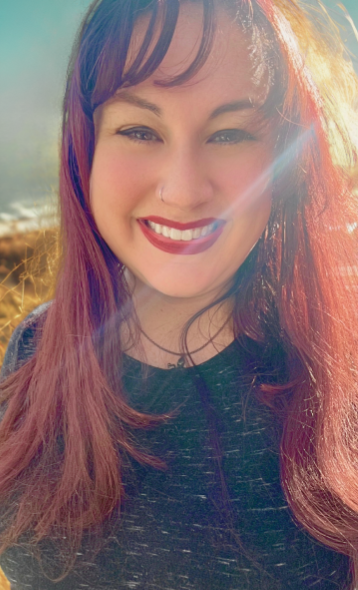 A picture of Lisa, a woman with auburn hair, red lipstick, a black shirt, and an octopus necklace in front of an outdoor setting.